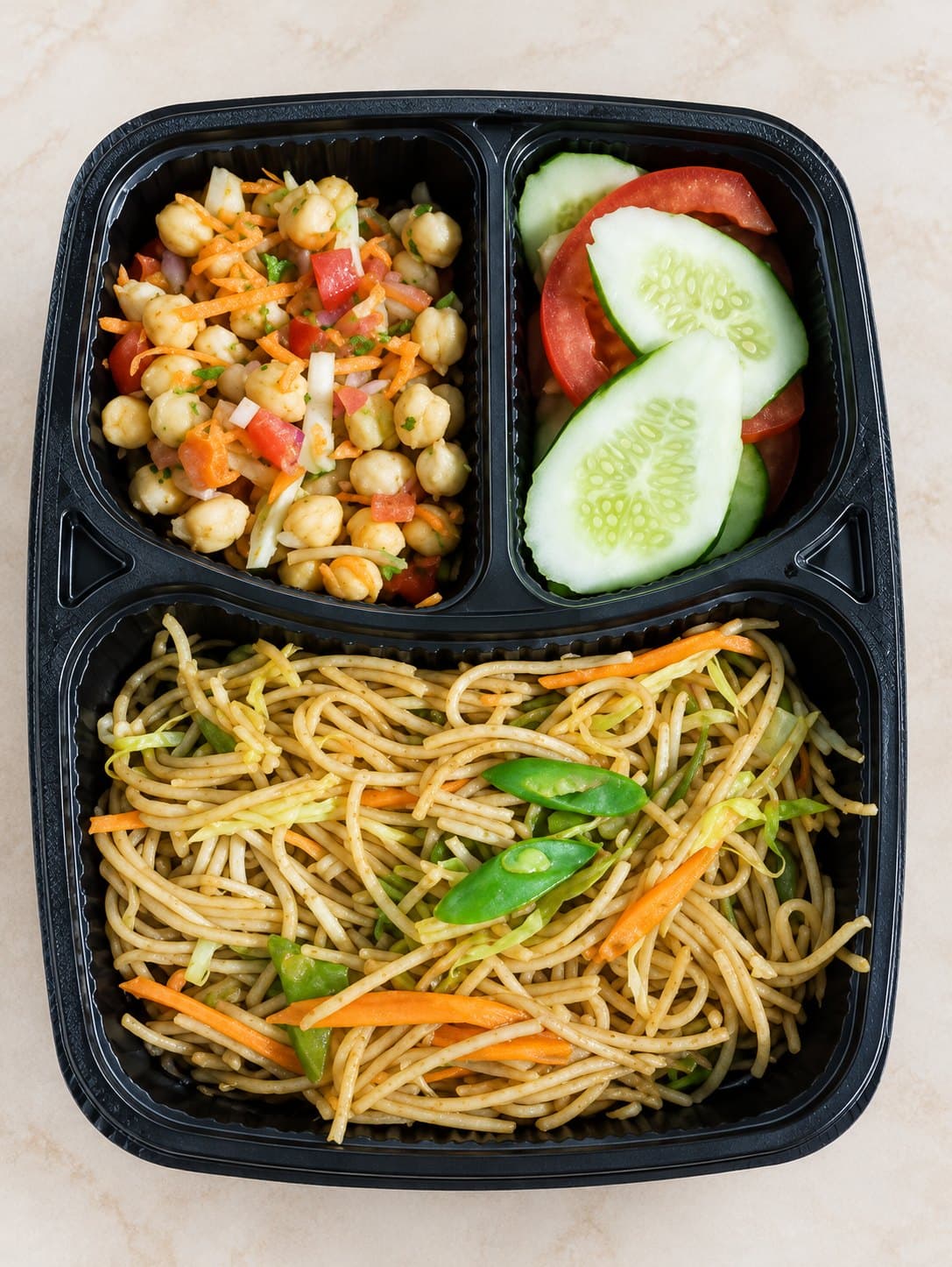 A real Kefilo veg three-compartment tray: vegetable noodles, a chickpea and vegetable side, and fresh cucumber and tomato salad